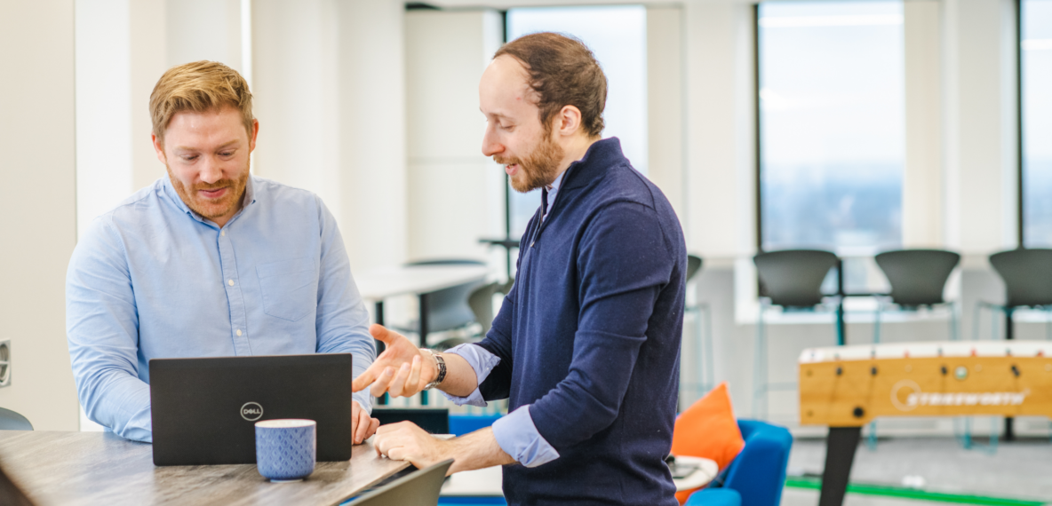 Two people having a conversation, looking at a laptop at a table in an office