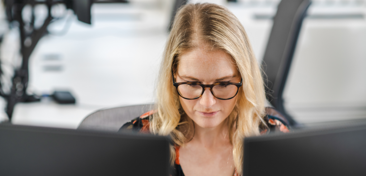 A person wearing glasses looking at two desktop computer screens