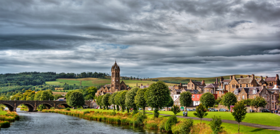 A cloudy day in a picturesque area with greenery, a river, and buildings